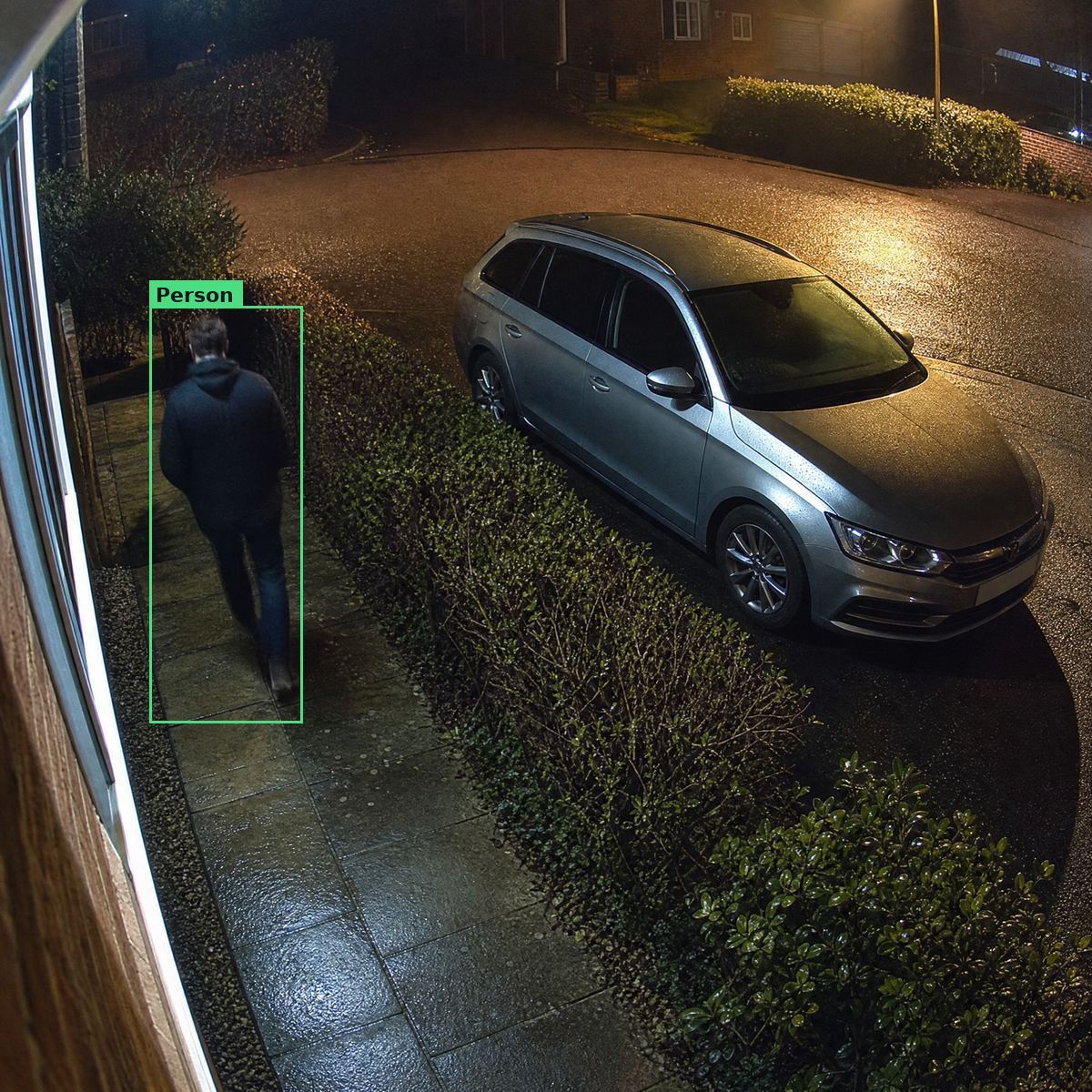 The view from a front window at night: a person on the path, a driveway and a parked car in colour